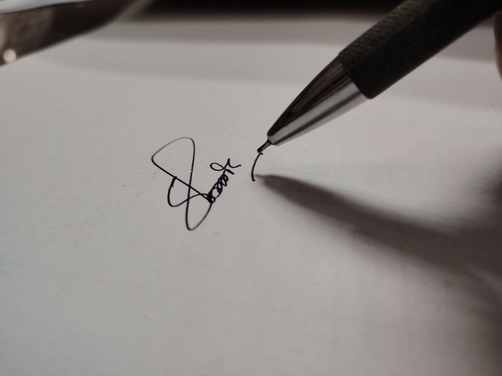 Macro shot of a pen writing a signature on white paper, emphasizing precision.