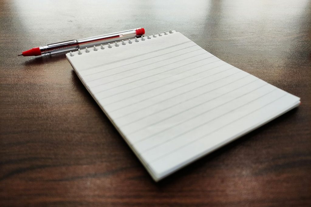 A lined notebook with a red pen on a wooden desk, perfect for school or office use.